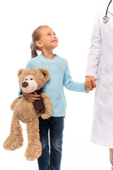 Girl with soft toy holding hand and smiling at pediatrician isolated on white