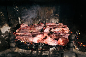 Grilled meat in the fireplace of his home. Raw beef on a barbecue grill with the coals underneath.