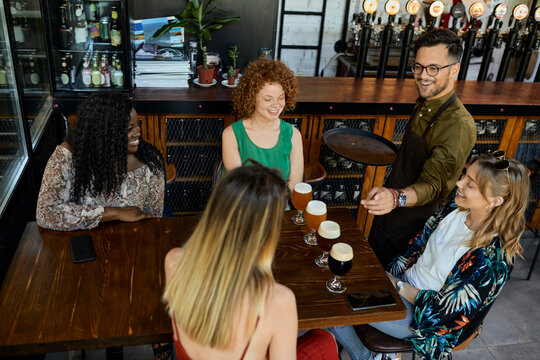 Waiter serving craft beer for female friends in a pub