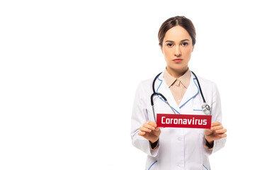 Fototapeta premium Doctor in white coat holding card with coronavirus lettering isolated on white