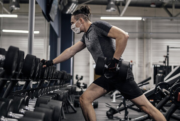Fototapeta na wymiar Pandemic gym - man working out with protective face mask during coronavirus outbreak