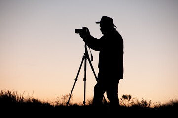 Silhueta de fotógrafo com chapéu e tripé ao pôr-do-sol