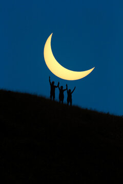 Silhouette of friends standing on mountain underneath eclipse