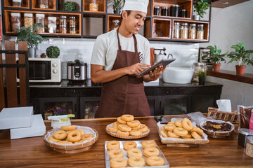 Fototapeta na wymiar Chef male prepare orders of donuts in the kitchen. The professional male holds a tablet digital at the kitchen