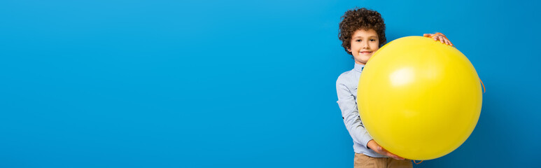 panoramic crop of pleased boy holding big yellow balloon on blue © LIGHTFIELD STUDIOS