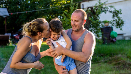 Photo of a happy family having fun outdoors. Father, mother and son are spending time together. Portrait of happy family outdoors in nature. Mom and dad are kissing their cute little son. Copy space.