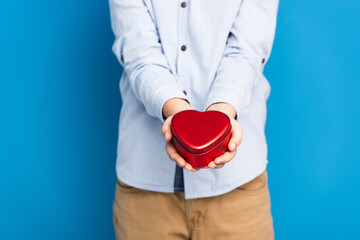 cropped view of boy holding red heart shape box on blue