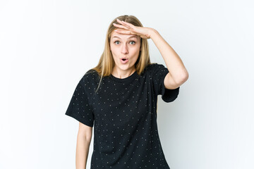 Young blonde woman isolated on white background looking far away keeping hand on forehead.