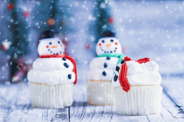 Iced Christmas Snowman cupcake with part bitten off or eaten. Other snowmen with carrot nose, Santa hat, and scarf. Selective focus with blurred background.