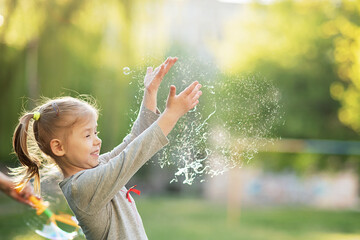 Emotional portrait of happy and active little beautiful girl bursting with soap bubbles laughing