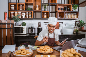 Fototapeta na wymiar male chef smiled as he counted the donuts and used his laptop for online marketing of his homemade products