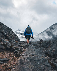 Man in a blue jacket with a backpack and a camera in his hand hiking in the mountains