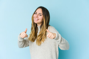 Young caucasian woman isolated on blue background raising both thumbs up, smiling and confident.