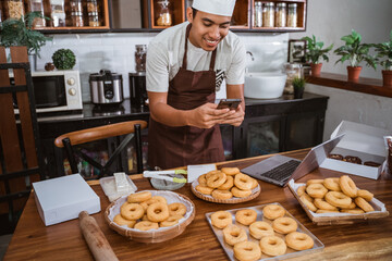 Fototapeta na wymiar male chef smiles while taking pictures of donuts using a smartphone for online marketing of homemade products