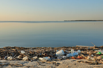 Landscape of polluted with plastic garbage shore of the lake on the sunset. Environmental disaster...