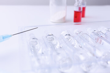 Syringe and a row of vials of medicine on a white table. Horizontal composition. Foreground.