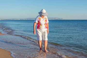 An elderly woman walks along the seashore. Summer vacation at the sea.