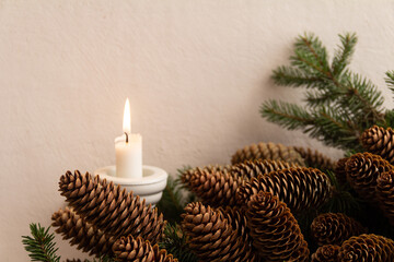 Christmas composition of a white candle in a white candlestick on a background of fir branches with cones