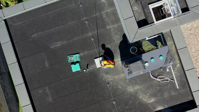 Caucasian Technician Wearing Orange Uniform and Hard Hat Installing Lightning Protection System Rod on Top of Commercial Building.