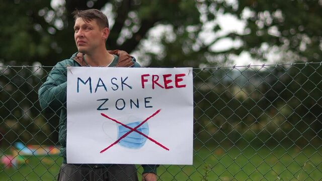 A poster on the fence with the inscription Mask Free Zone. A young male activist comes up and takes off his mask. I hung it on the fence next to the poster. Anti-mask concept, covid-denier