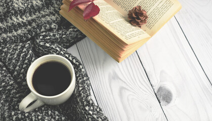 A cup of black coffee with book, flower and red autumn leaf with warm woolen clothes on the brown background. Flat lay, top view, copy space. Autumn cozy composition, fall concept.