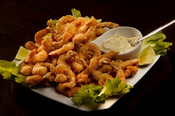 breaded shrimp with lettuce leaves, pieces of lemon tahiti and mayonnaise, on a white plate, on wooden table