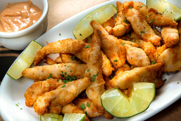 Breaded Fish Steaks Appetizer with Lemon Slices on a White Platter and Pot with Special Sauce
