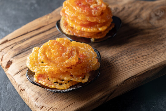 Indian sweets jalebi on a wooden on a dark background. Powdered sugar is poured on top.