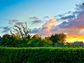 Naklejka na ściany i meble Divine azure sky with sunset clouds colored in purple beige tones over satured green landscape