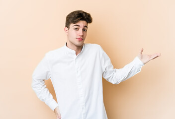 Young caucasian man isolated on beige background doubting and shrugging shoulders in questioning gesture.