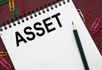 Design concept - Top view of white spiral notebook and pencil with text ASSET isolated on red background for mockup