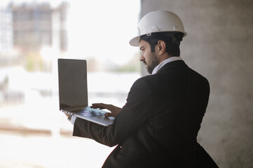 Man in suit and safety helmet works on laptop