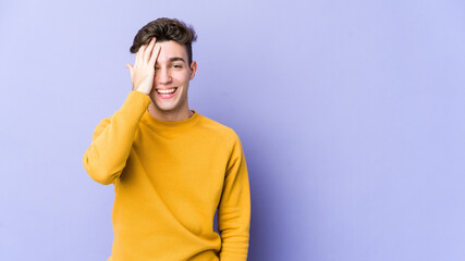 Young caucasian man isolated on purple background having fun covering half of face with palm.