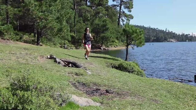 Mujer corriendo cerca de un lago al aire libre en la montaña, haciendo entrenamiento de resistencia. Estilo de vida saludable y disciplina deportiva