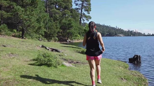 Mujer corriendo cerca de un lago al aire libre en la monta&ntilde;a, haciendo entrenamiento de resistencia. Estilo de vida saludable y disciplina deportiva