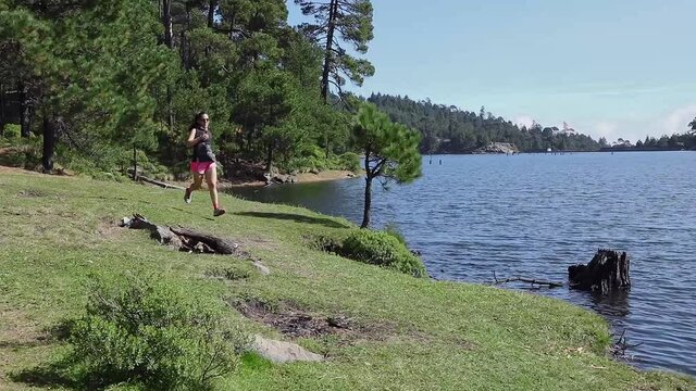 Mujer corriendo cerca de un lago al aire libre en la monta&ntilde;a, haciendo entrenamiento de resistencia. Estilo de vida saludable y disciplina deportiva