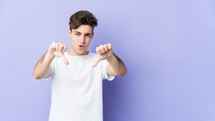 Young caucasian man isolated on purple background showing thumb down and expressing dislike.