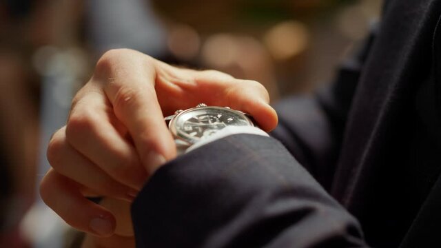 Unrecognizable man looking at wrist watch in park. Guy hiding watch under sleeve