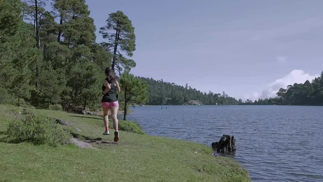 Mujer corriendo cerca de un lago al aire libre en la monta&ntilde;a, haciendo entrenamiento de resistencia. Estilo de vida saludable y disciplina deportiva