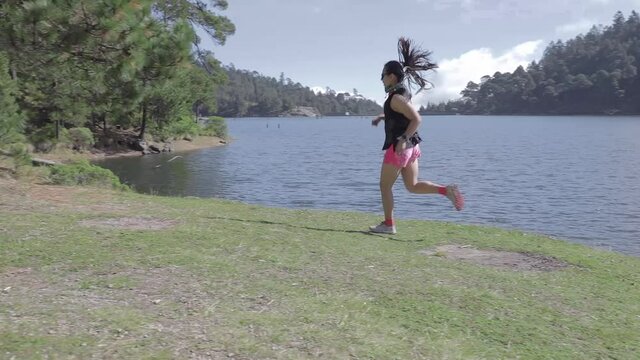Mujer joven de trail running cerca de un lago al aire libre en la monta&ntilde;a, haciendo entrenamiento de resistencia. Estilo de vida saludable y disciplina deportiva