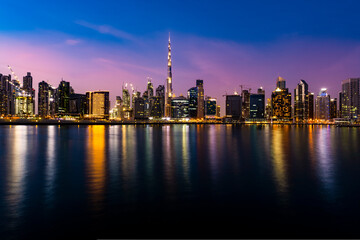 Fototapeta na wymiar Stunning view of the illuminated Dubai skyline at dusk with the magnificent Burj Khalifa reflected on the water canal flowing in the foreground. 