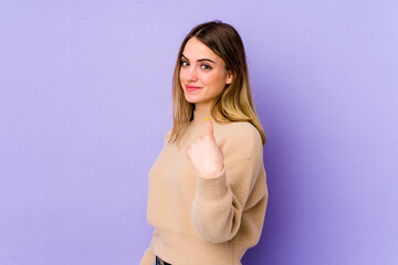 Young caucasian woman isolated on purple background pointing with finger at you as if inviting come closer.