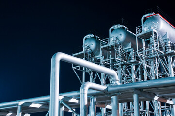 Pipelines in several rows and different configurations to a processing plant at night.