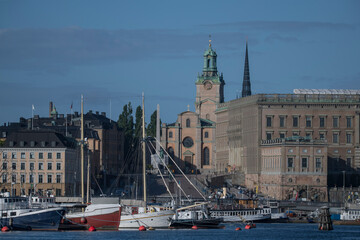 Fototapeta premium Boats at the jetties at the bridge between Blasieholmen and Skeppsholmen in Stockholm a sunny summer morning, old houses, the church Storkyrkan and the Royal Castle in the old town
