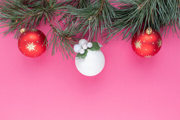 Flat lay with festive pine tree branch and christmas decorations on pink background.