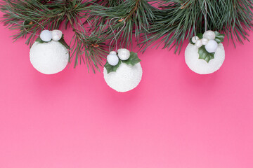 Flat lay with festive pine tree branch and christmas decorations on pink background.