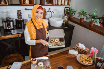 beautiful woman in scarf smiling happily in the kitchen preparing donuts and packing them into donut boxes