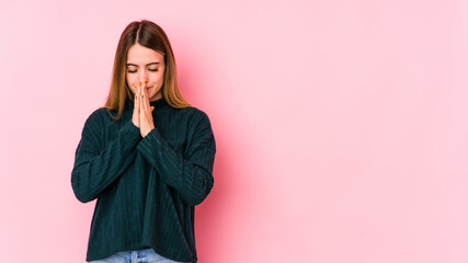 Young caucasian woman isolated on pink background praying, showing devotion, religious person looking for divine inspiration.