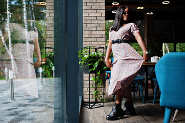 Fashion portrait of african american woman in long dress, boots and sunglasses indoor.