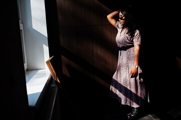 Game with shadows. Fashion portrait of african american woman in long dress and eyeglasses indoor.